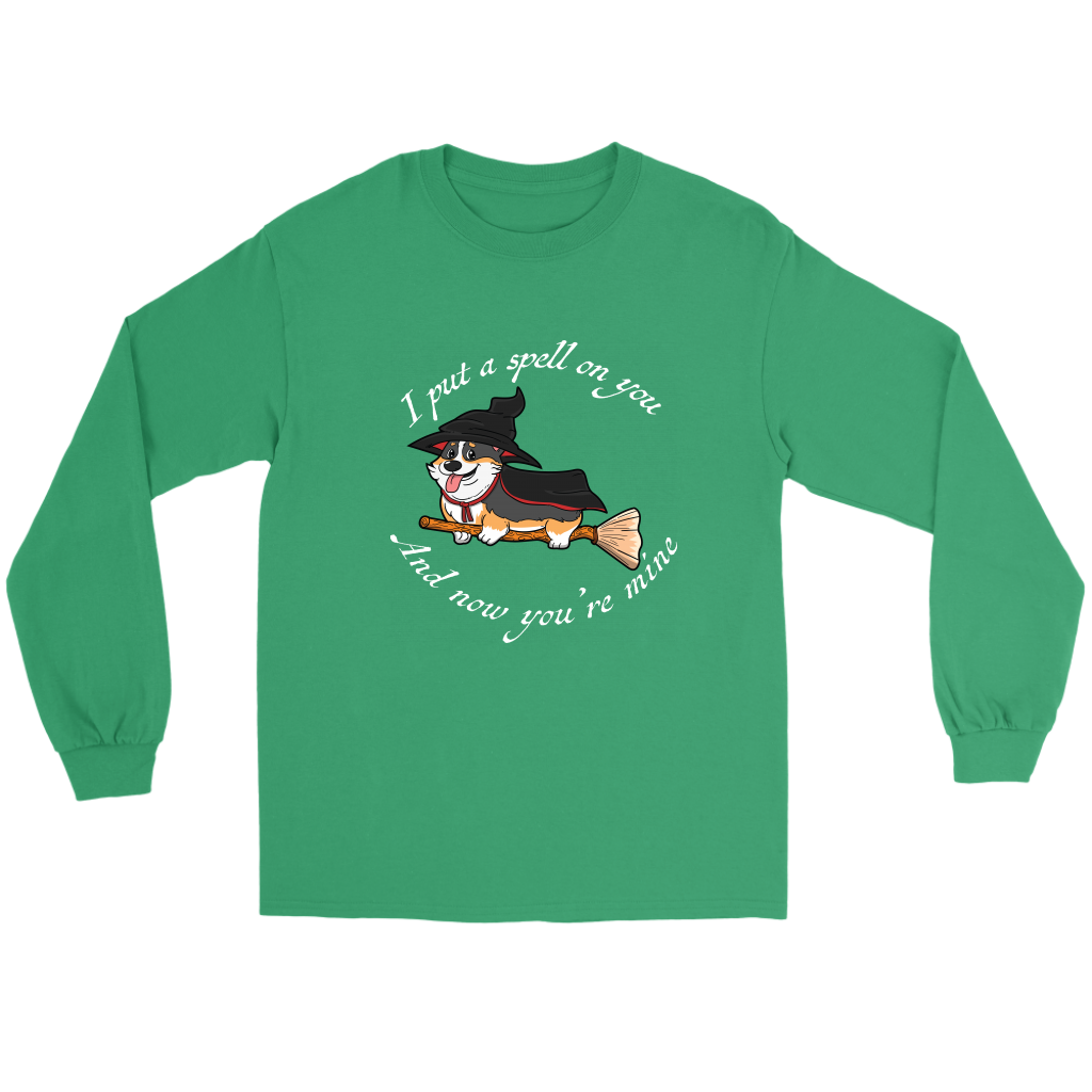 A flat lay of a long sleeved t shirt. The shirt is green and has white text that says: I put a spell on you and now you're mine. There is also a tricolor corgi dressed as a witch while riding a broom.