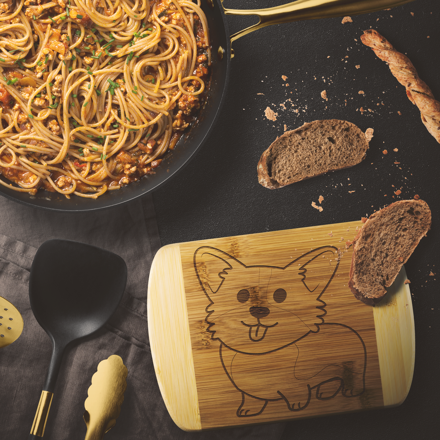 Picture of bamboo cutting board with corgi design etched in, sitting next to a delicious looking pan of pasta and some rustic bread.