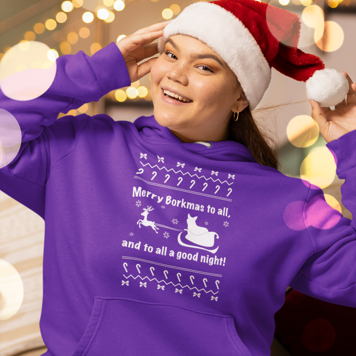 A model wearing a purple hoodie with the text "Merry Borkmas to all, and to all a good night!" with a corgi in Santa's sled.