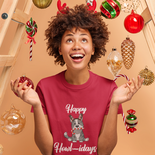 A model wearing a red shirt that has a cardigan corgi on it. The corgi is wearing fake reindeer horns and is holding a candy cane in its mouth. The text says 
