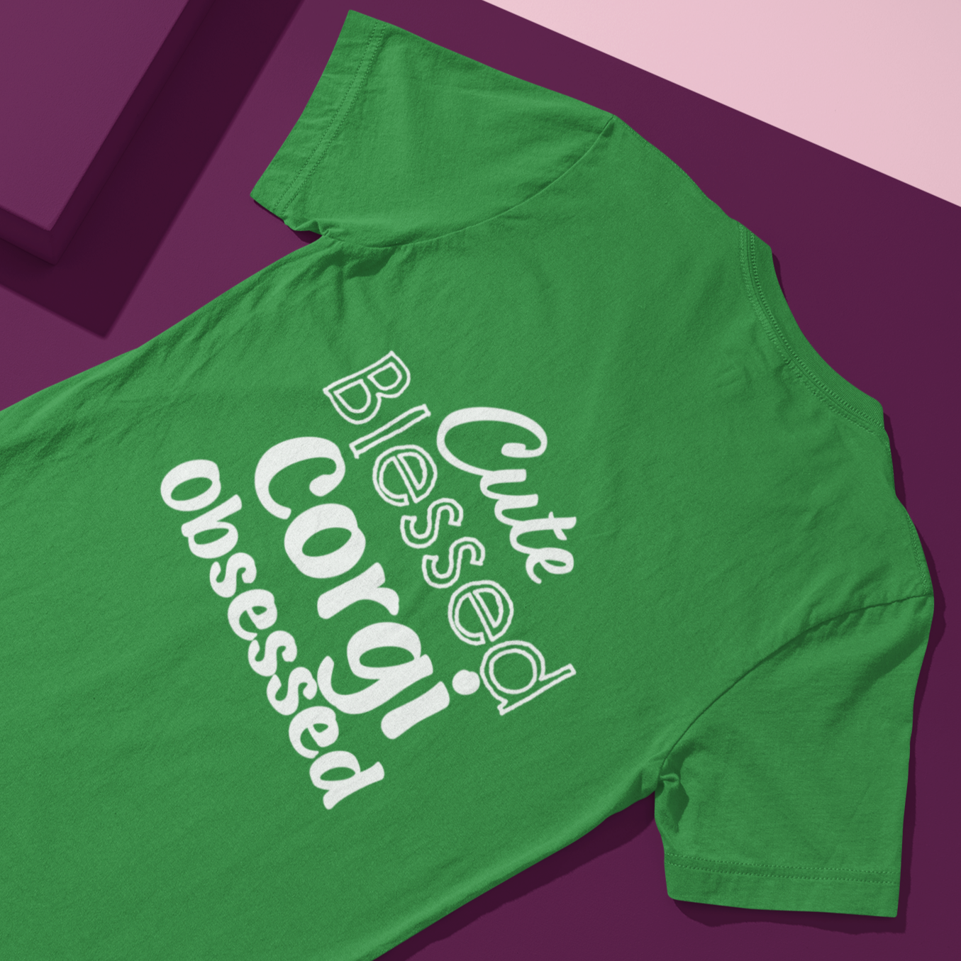 A flat lay of a t shirt with white text "Cute Blessed Corgi Obsessed". The shirt is lying on a purple backdrop. 