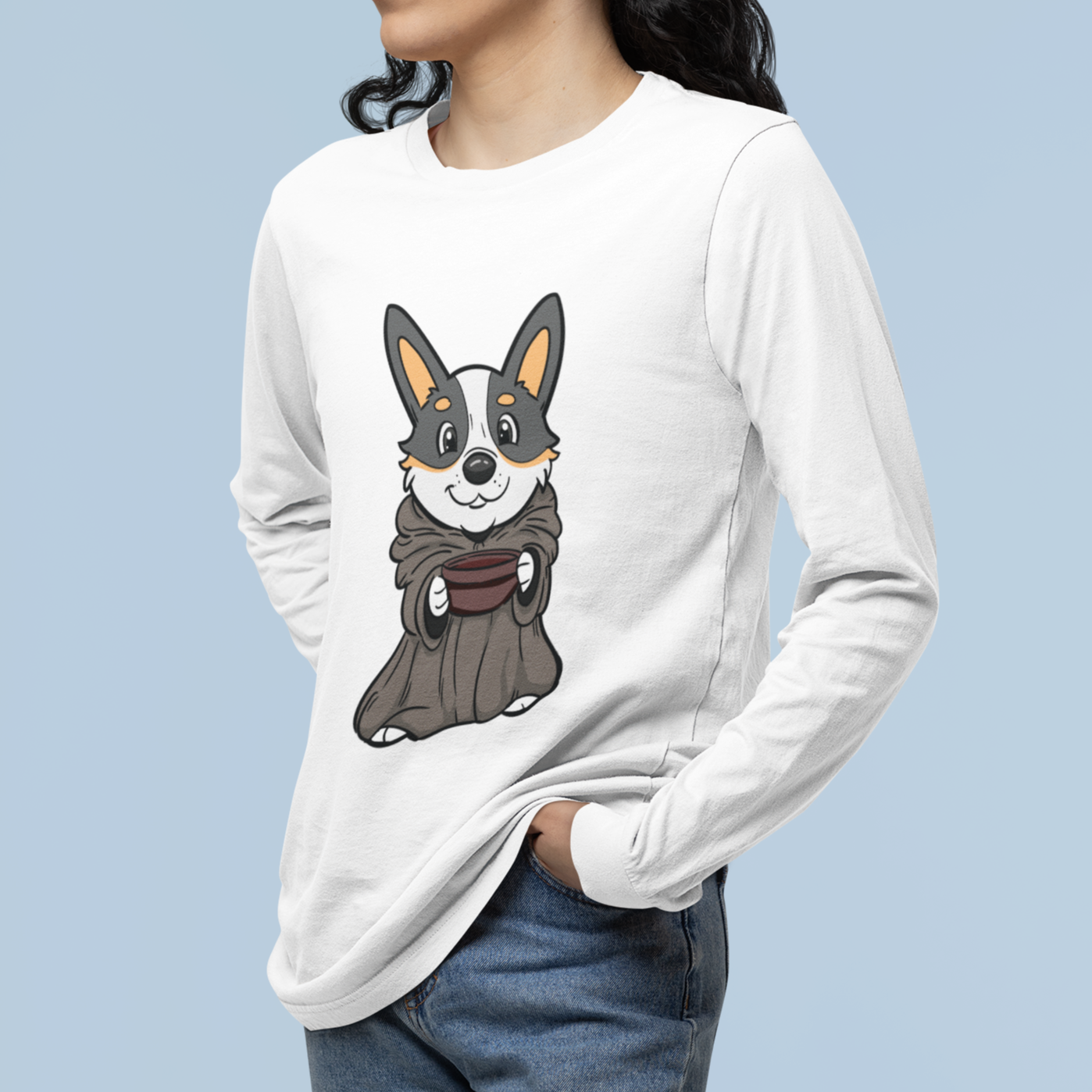 I model wearing a white long sleeved T shirt. The design of the shirt is a tricolor corgi that is dressed up as baby Yoda, (Grogu), from the Mandalorian. 