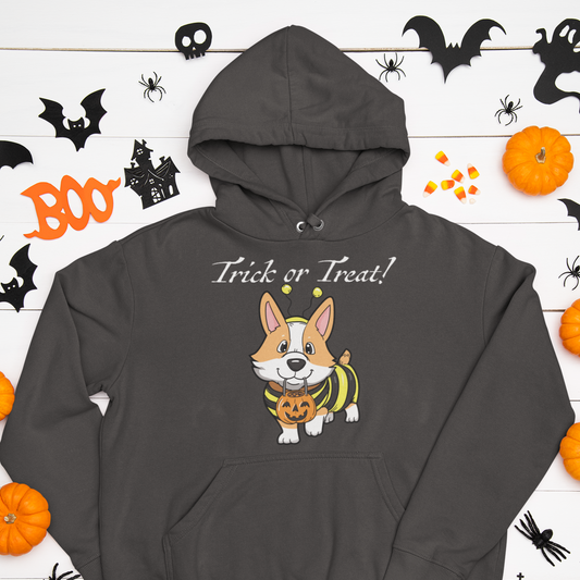 A hooded sweatshirt on a table with some cut out halloween decorations like ghosts and bats. The hoodie has a fawn corgi wearing a bumblebee costume with the text "Trick or Treat!". Hoodie is dark grey.