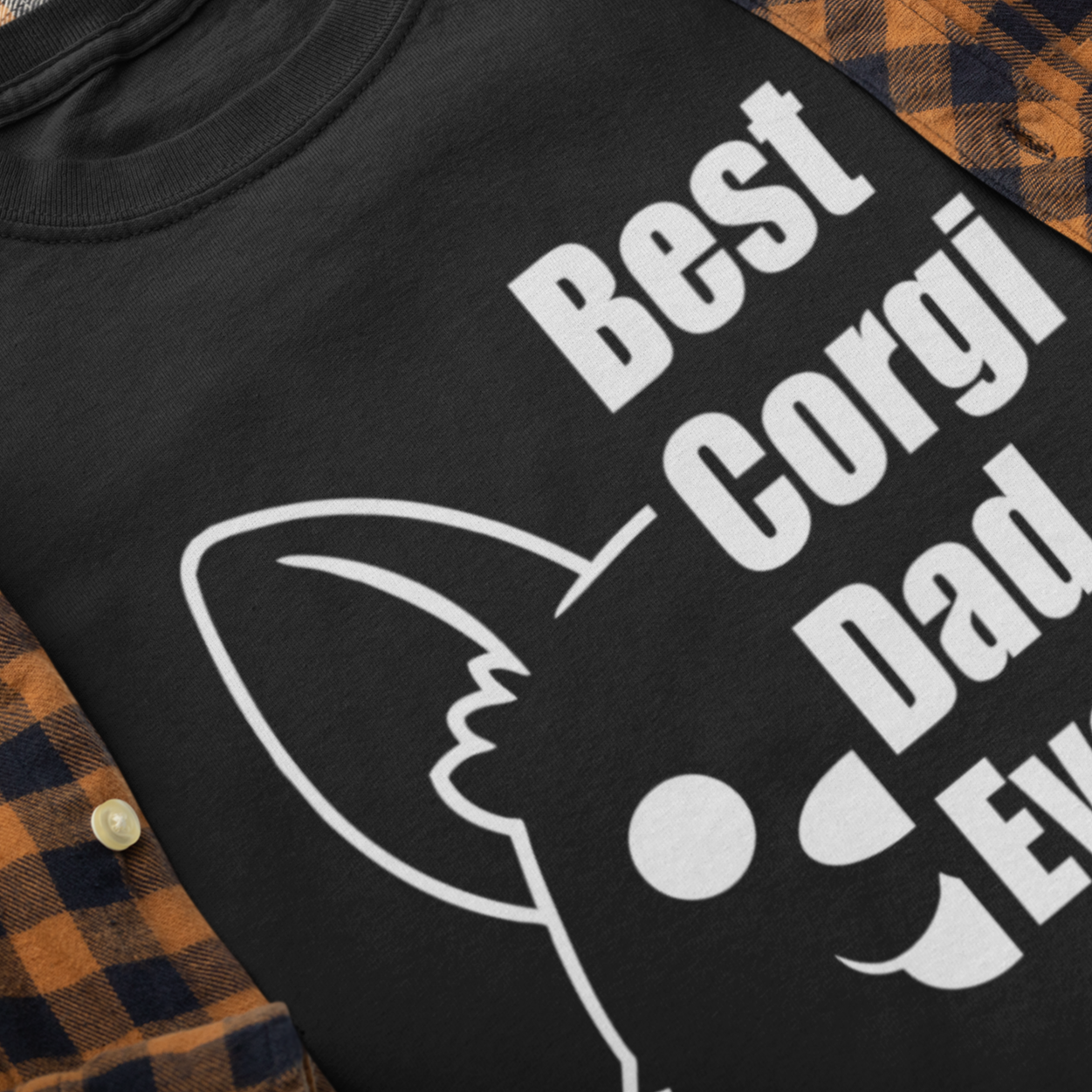 A flat lay of a black t shirt inside of a orange and black flannel shirt. Black shirt with half of a corgi's face and the text "Best corgi dad ever"