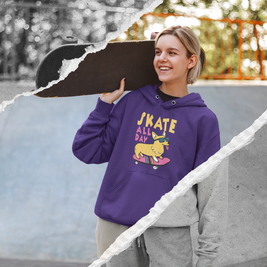 A model is wearing a purple hooded sweatshirt. There's yellow and pink text that says "Skate all day" and there's a a corgi wearing sunglasses riding on a skateboard. The model is holding a skateboard and appears to be standing at a skate park. 