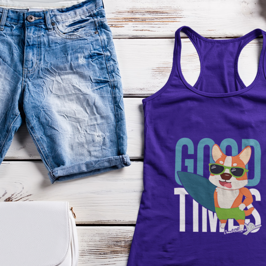 A purple tank top sitting on a white table next to a pair of shorts and a purse. The tank top has blue and white writing that says "Good times, Good vibes". In the foreground on the shirt, there's a corgi wearing swim trunks and sunglasses. The corgi is holding a surfboard. 