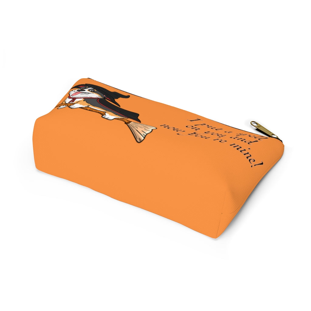 An orange make up bag with a pattern of a tricolor corgi dressed in a witch's halloween costume, on a broom. With the text "I put a spell on you and now you're mine". This picture shows the bottom of the bag.