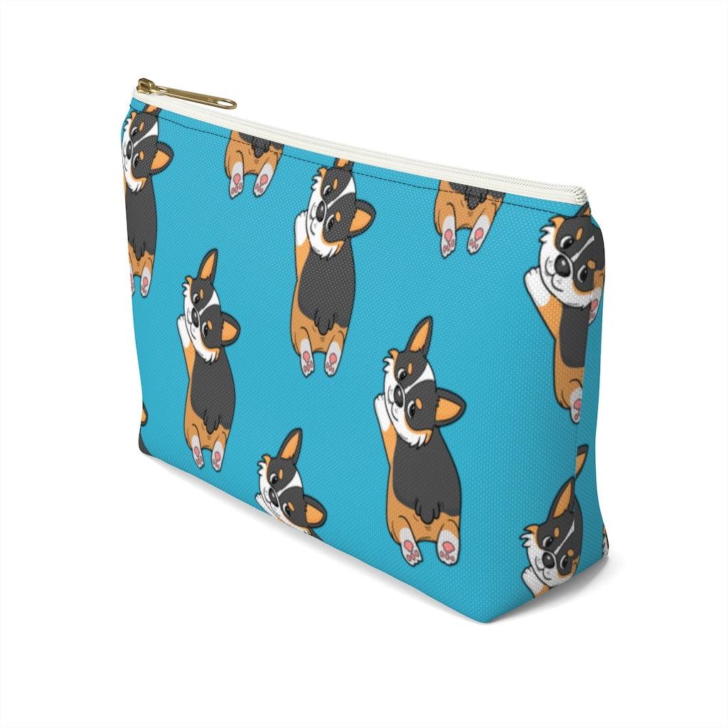 A blue make up bag with a pattern of a tricolor corgi splooting.