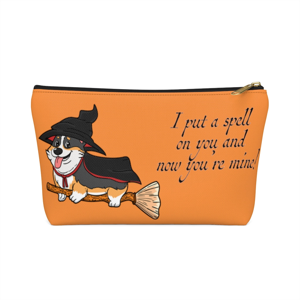 An orange make up bag with a pattern of a tricolor corgi dressed in a witch's halloween costume, on a broom. With the text "I put a spell on you and now you're mine".