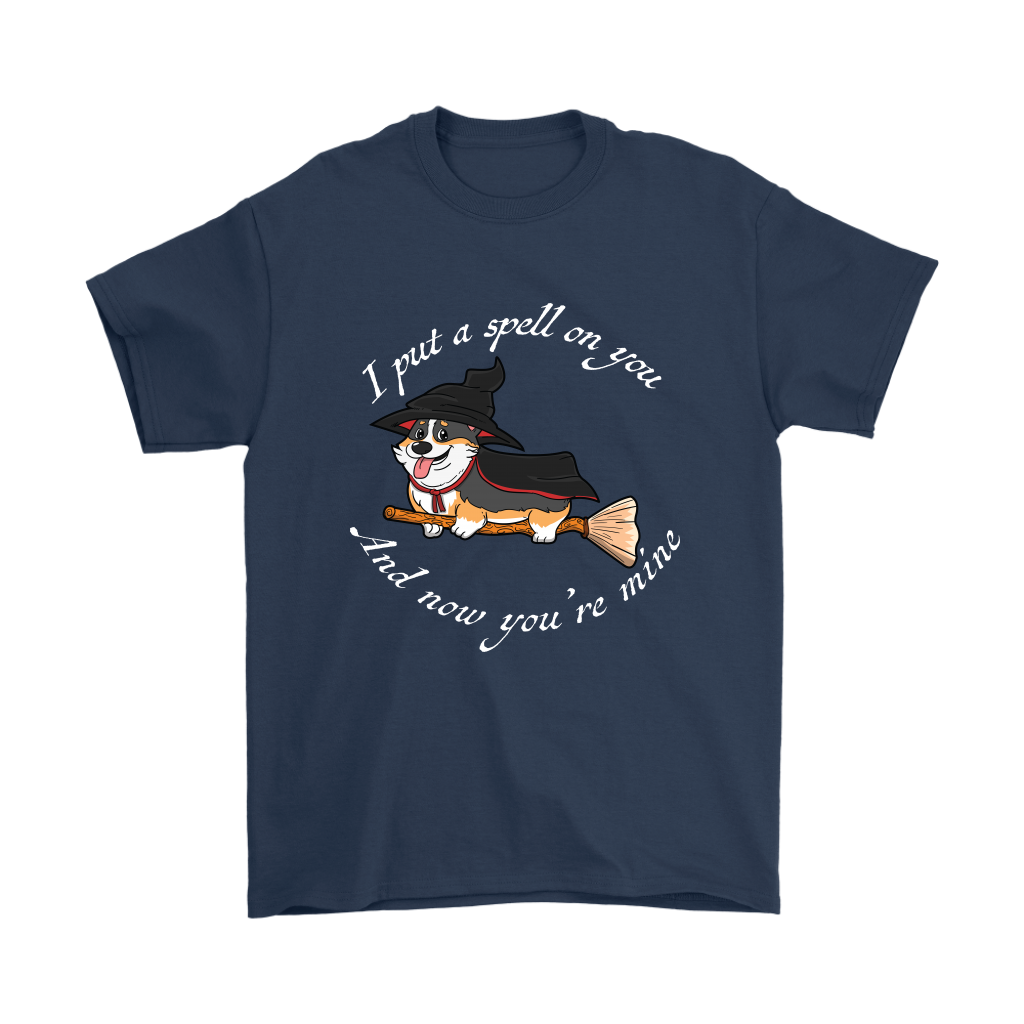 A t shirt with a tricolor corgi wearing a witch costume while riding a broom. The text says "I put a spell on you and now you're mine" and the shirt is dark blue.