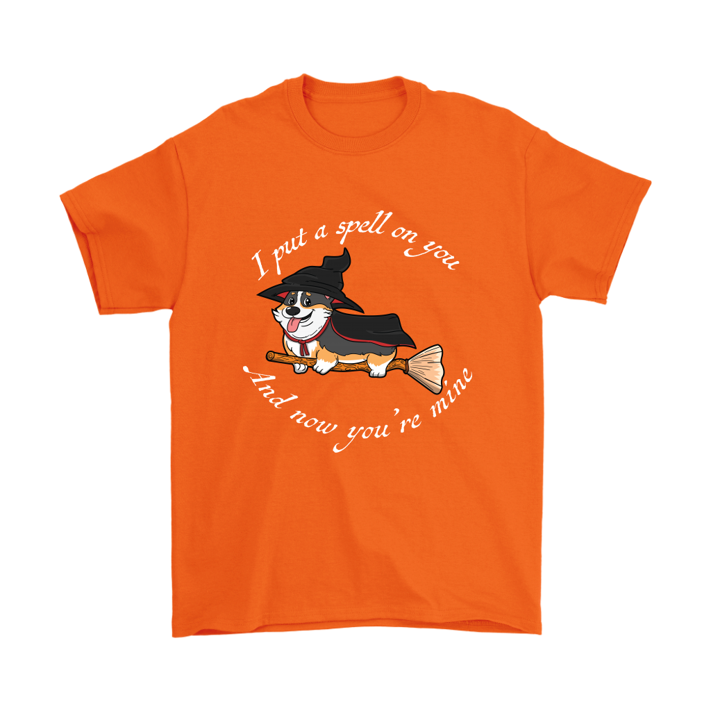 A t shirt with a tricolor corgi wearing a witch costume while riding a broom. The text says "I put a spell on you and now you're mine" and the shirt is orange.