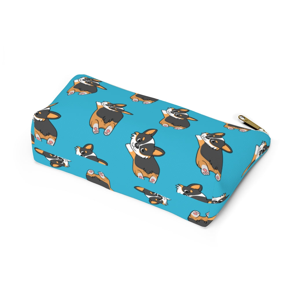 A blue make up bag with a pattern of a tricolor corgi splooting.