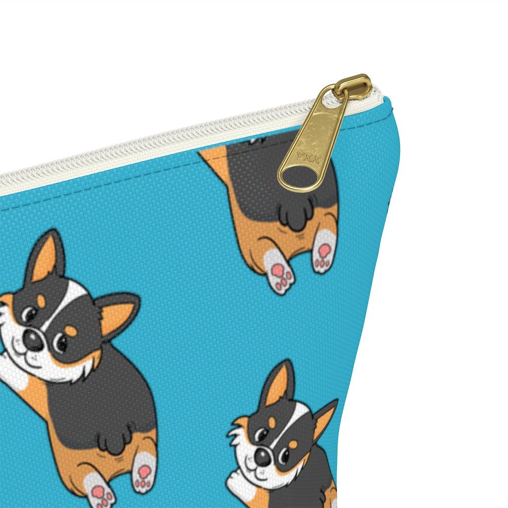 A blue make up bag with a pattern of a tricolor corgi splooting.