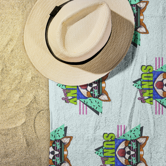 The sunny days beach towel on some sand with a hat on the corner.