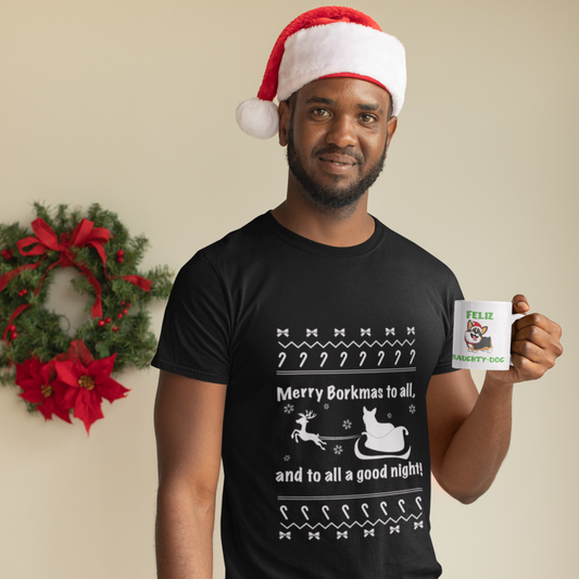 A model wearing a black, short sleeved shirt that says  "Merry Borkmas to all, and to all a good night!" with a Christmas pattern, and a corgi in Santa's sleigh. The model is standing in front of a wreath and he's wearing a Santa hat. He's holding a mug with our Feliz Naught-Dog design on it. 