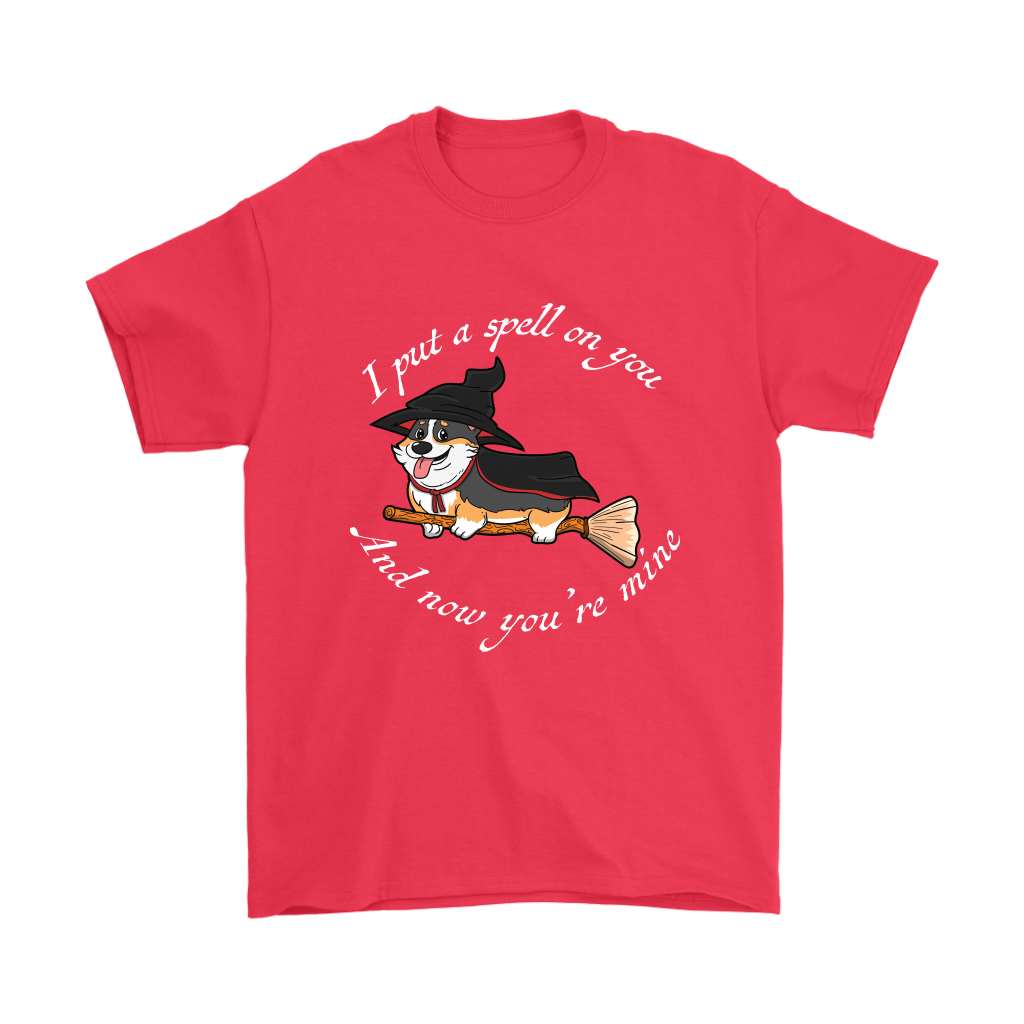 A t shirt with a tricolor corgi wearing a witch costume while riding a broom. The text says "I put a spell on you and now you're mine" and the shirt is red.