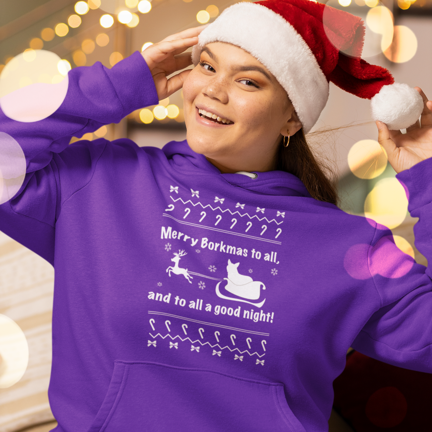 A model wearing a purple hoodie with the text "Merry Borkmas to all, and to all a good night!" with a corgi in Santa's sled. 