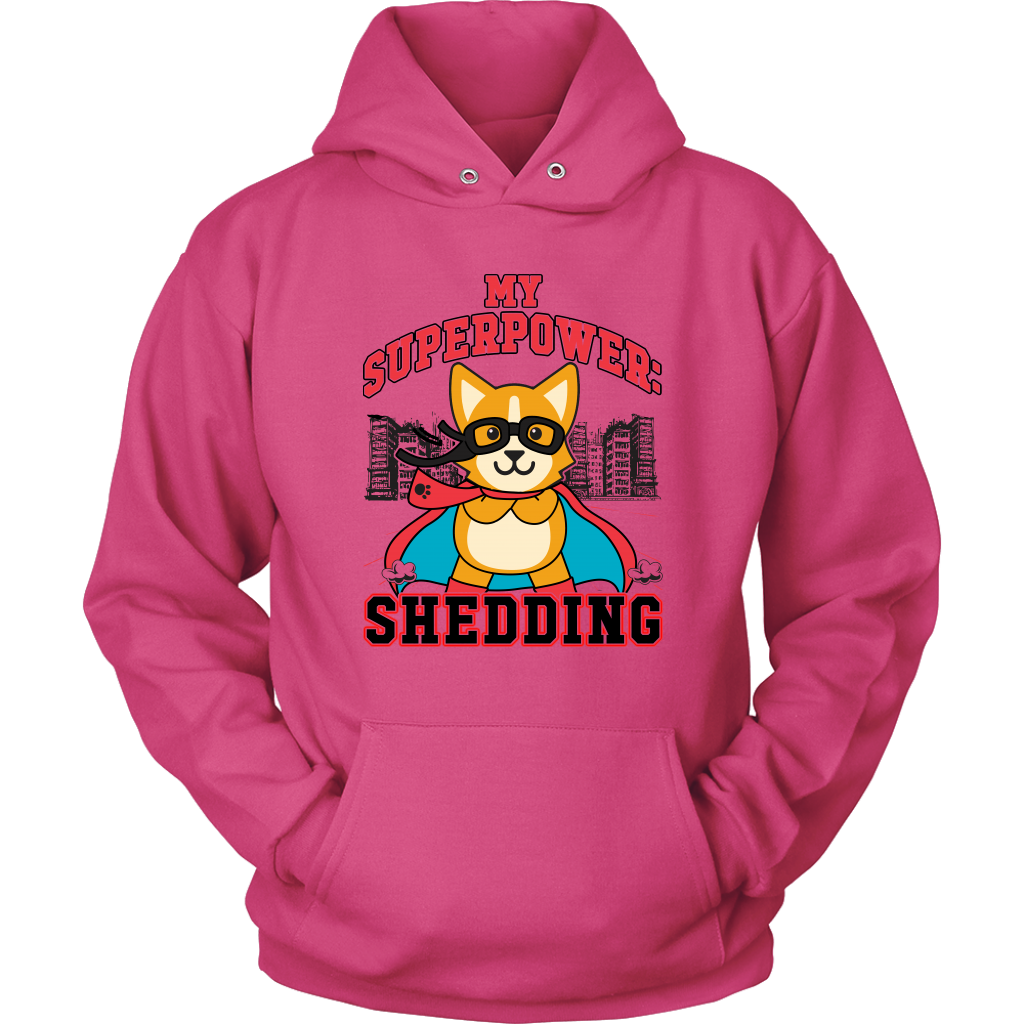 A flay lay of a hoodie that is pink and has red and black text that says "My superpower: Shedding" with a corgi dressed as a superhero. 