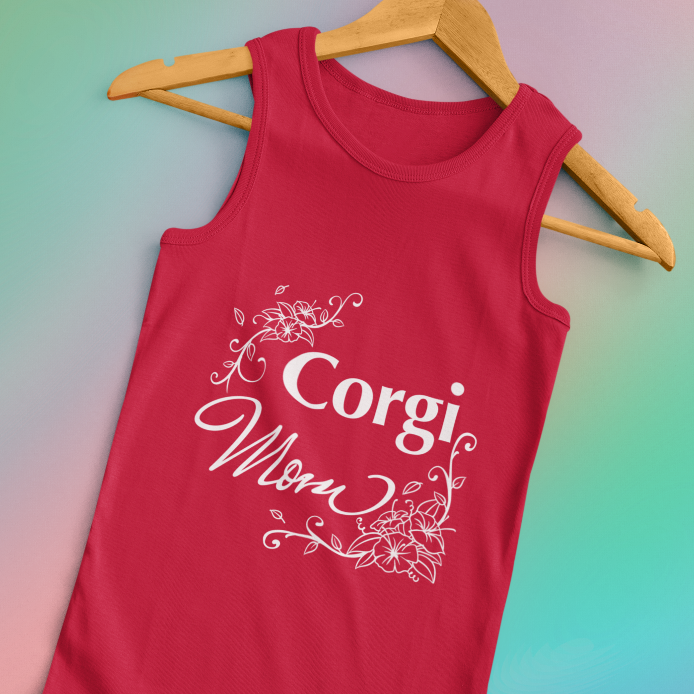 A unisex tank top hanging from a wooden hanger with the text "Corgi Mom" in flowery text. The tank top is red.