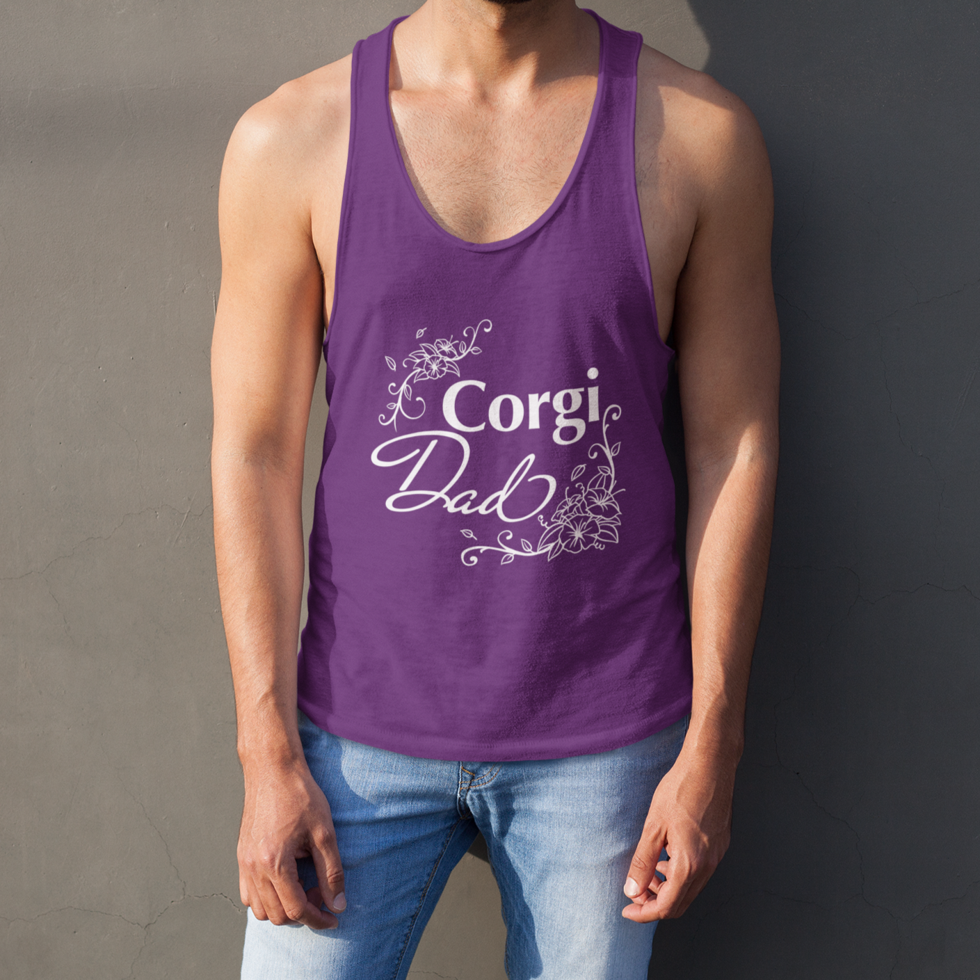 A model is standing against a wall wearing a racerback tank top with the text "Corgi Dad" in flowery text. The tank top is dark purple.