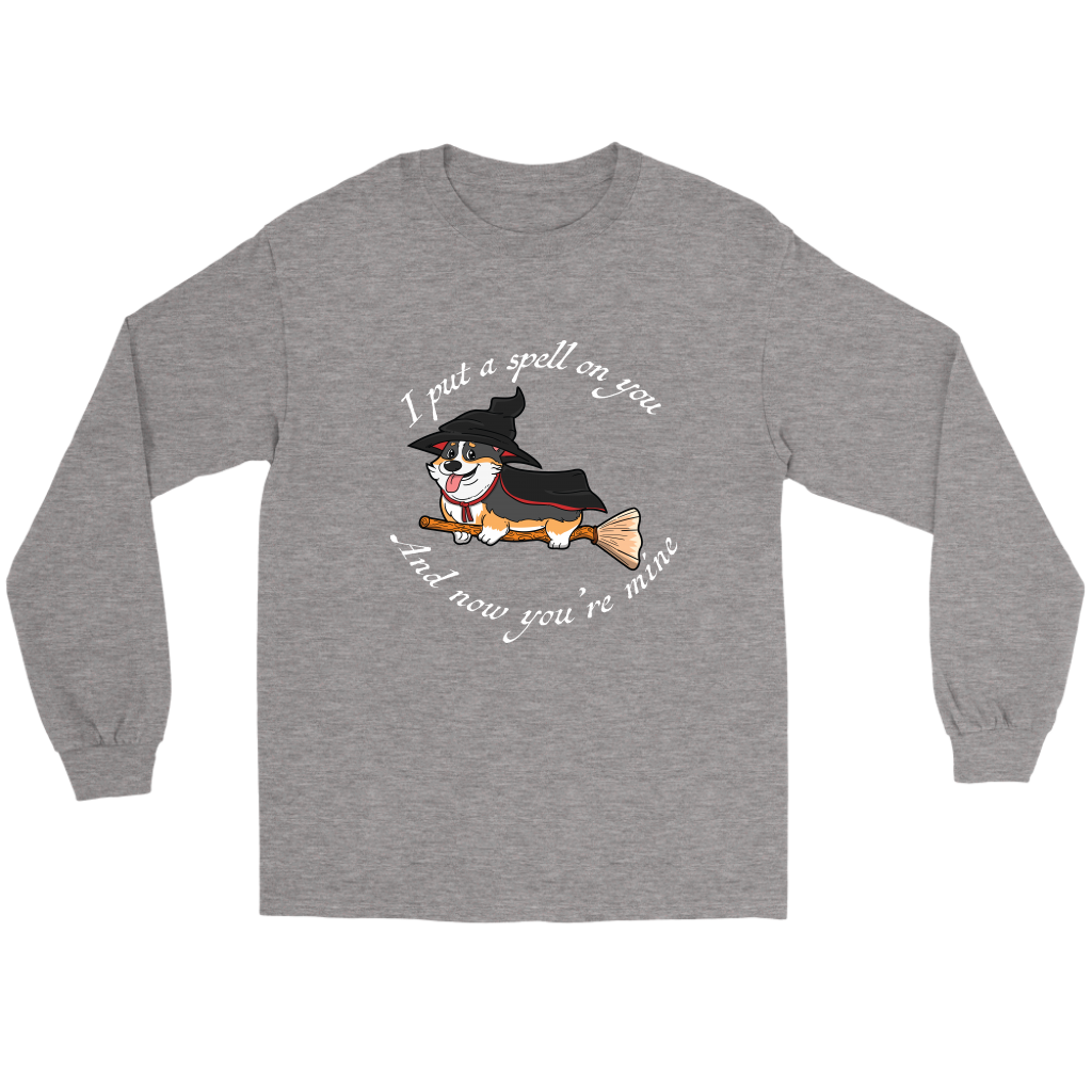 A flat lay of a long sleeved t shirt. The shirt is grey heather colored and has white text that says: I put a spell on you and now you're mine. There is also a tricolor corgi dressed as a witch while riding a broom. 