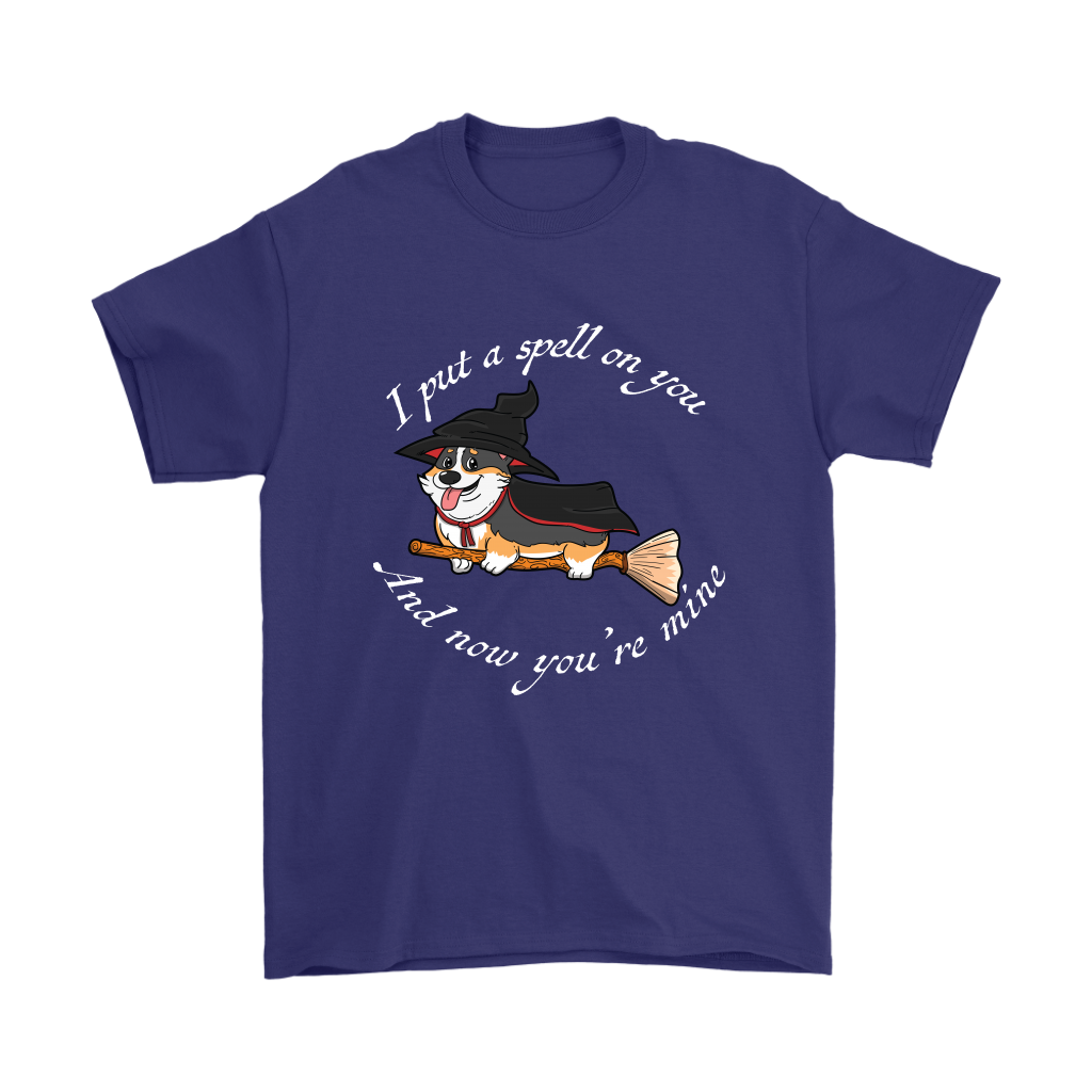 A t shirt with a tricolor corgi wearing a witch costume while riding a broom. The text says "I put a spell on you and now you're mine" and the shirt is purple.